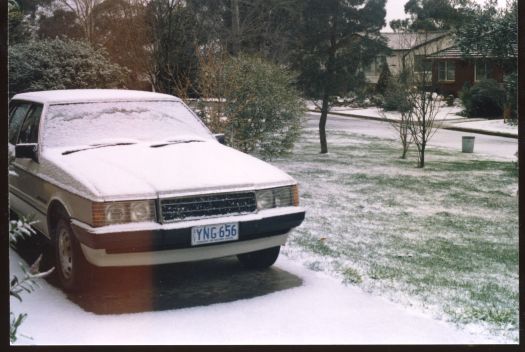 Unidentified scene showing snow on a car with ACT licence plates in a driveway in a suburb. The car appears to be a late 1970s or 1980s model.