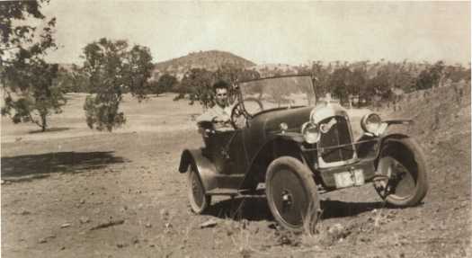 Jack Teasdale sitting in his two seater, two cylinder Citroen convertible on the paddocks near White City. Mt Ainslie in the background.