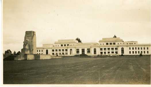 Off centre front view of Parliament House from the lawns. King George V memorial is at left and a bus is in front of the building.