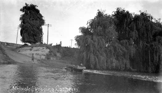 A car driving through the waters of the Molonglo River at Acton. Probably Lennox Crossing. A man is standing on the far side of the crossing.