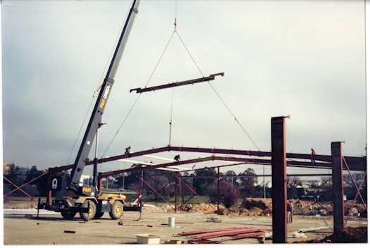 Crane lifting a girder during construction of a building. Parliament House is visible in the background.