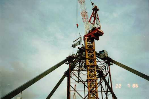View from below of a crane putting in place a curved section of one flag pole leg