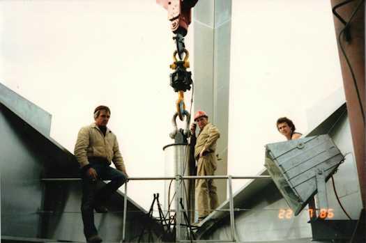 Three workmen standing next to the top of the mast as it is about to raised into place