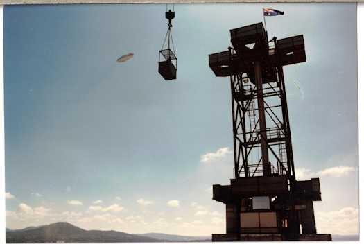 Crane and dog box being lifted by a crane. A zeppelin shaped balloon is away to the left.