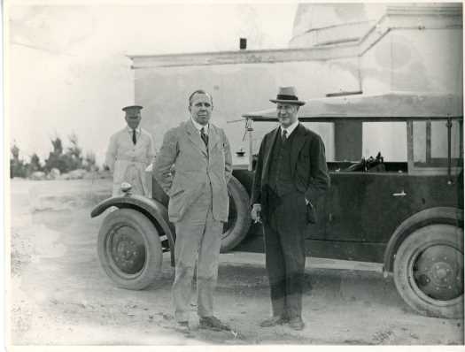 Duffield and (possibly) Goodwin standing in front of car and driver with observatory building behind.