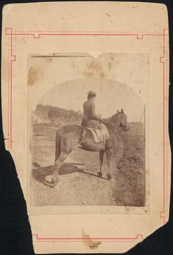 Isabelle McPherson riding a horse. Some buildings in background.
