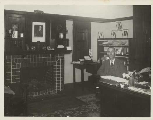Dr Tillyard at his desk showing fireplace and ornaments. Probably early 1930s.