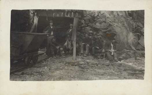 Seven workers and large bin on rail track at entrance to the tunnel.