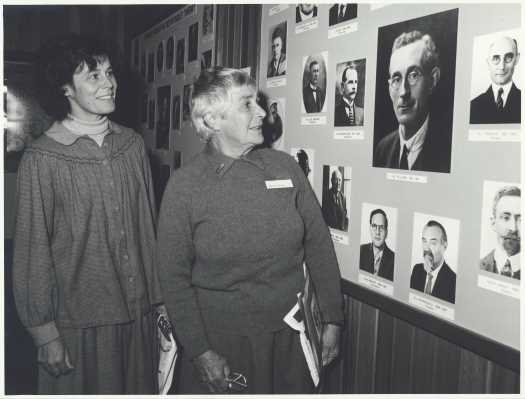 Faith Evans is inspecting photographs of people displayed in the exhibition 'Where would we be without them?' on 6 June 1982. It includes her father Dr Robin Tillyard. On the occasion of the opening of the new building to house the insect collection.