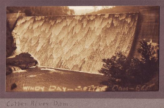 Windy day Cotter Dam FCT is written at the bottom. Water is flowing over the dam wall.