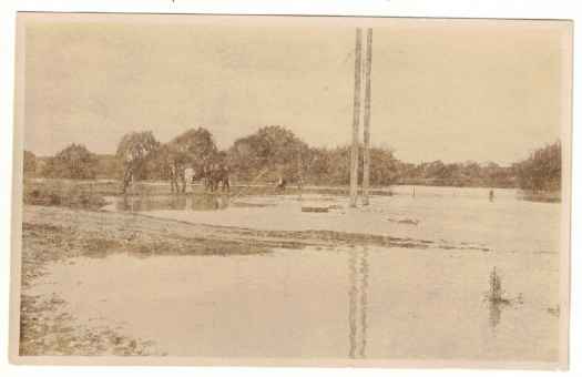 Possibly light rail crossing. Group of men in middle distance. River appears flooded.