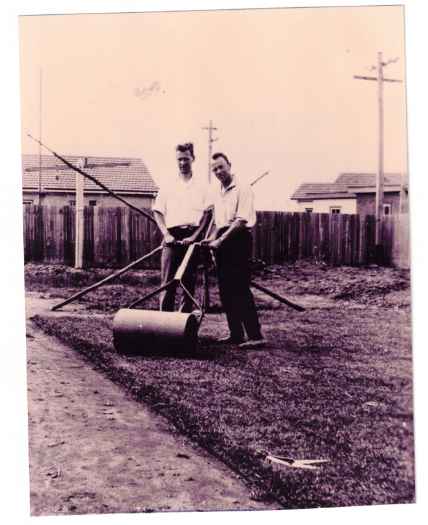 The two men are posing by a heavy lawn roller.