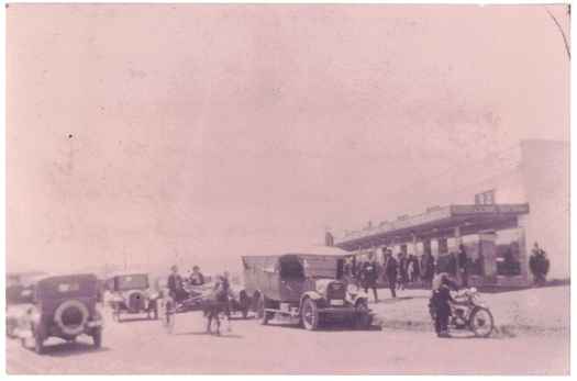Shops on the right and on the street are cars, truck, motor bike and horse and cart.
The shops were: JB Young, Dunn's news agency, SO Taylor, JG Gunn, motor shop and bowser.
