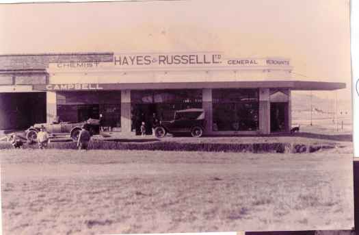 Hayes & Russell Ltd, general merchants and also Campbell's pharmacy. Vehicles parked outside.