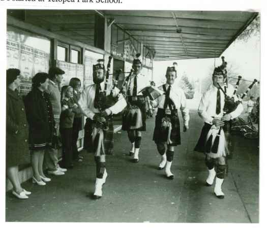 Four bagpipers march on street outside the bakery. 