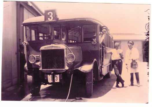 Two men are standing at the side of the bus (one a ticket collector) and one (driver) is on board.