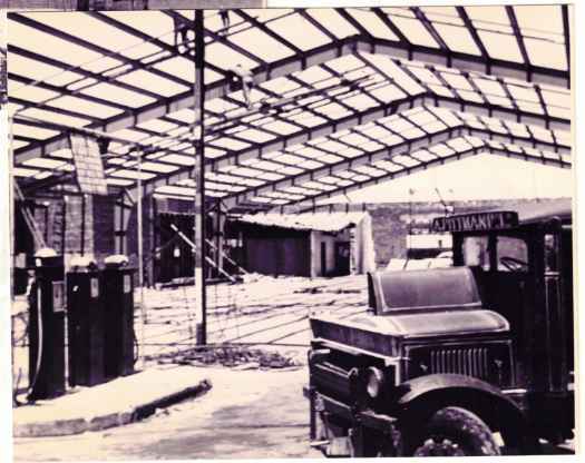 Roof taking shape from inside. Truck with 'A. Pittman Ltd' sign. Petrol bowsers visible.