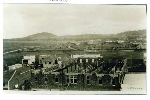 Taken from the Capitol Theatre. Built up to second floor but no roof yet. Bottom right is A.M. Innes sign (Capitol Cafe - now Caphs 2026). No buildings between Bougainville Street and Murray Crescent.