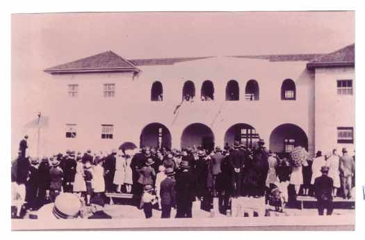 Large crowd gathered in front of the school, some standing on benches