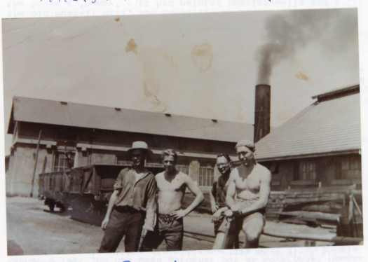 Four workers in front of a shed that is in front of the Fitters Workshop. Rail wagons and timber evident.
