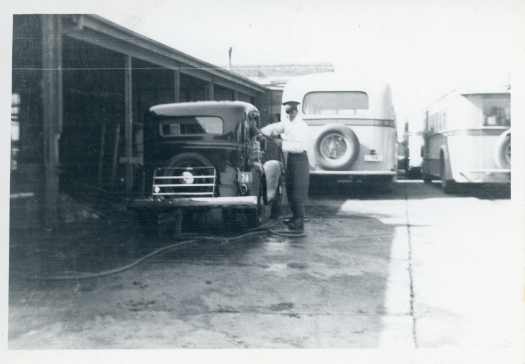 Stan Rowe is washing Harry Knight's car (Rego 74) in the Transport Depot before the roof was constructed. Two busses in background. 